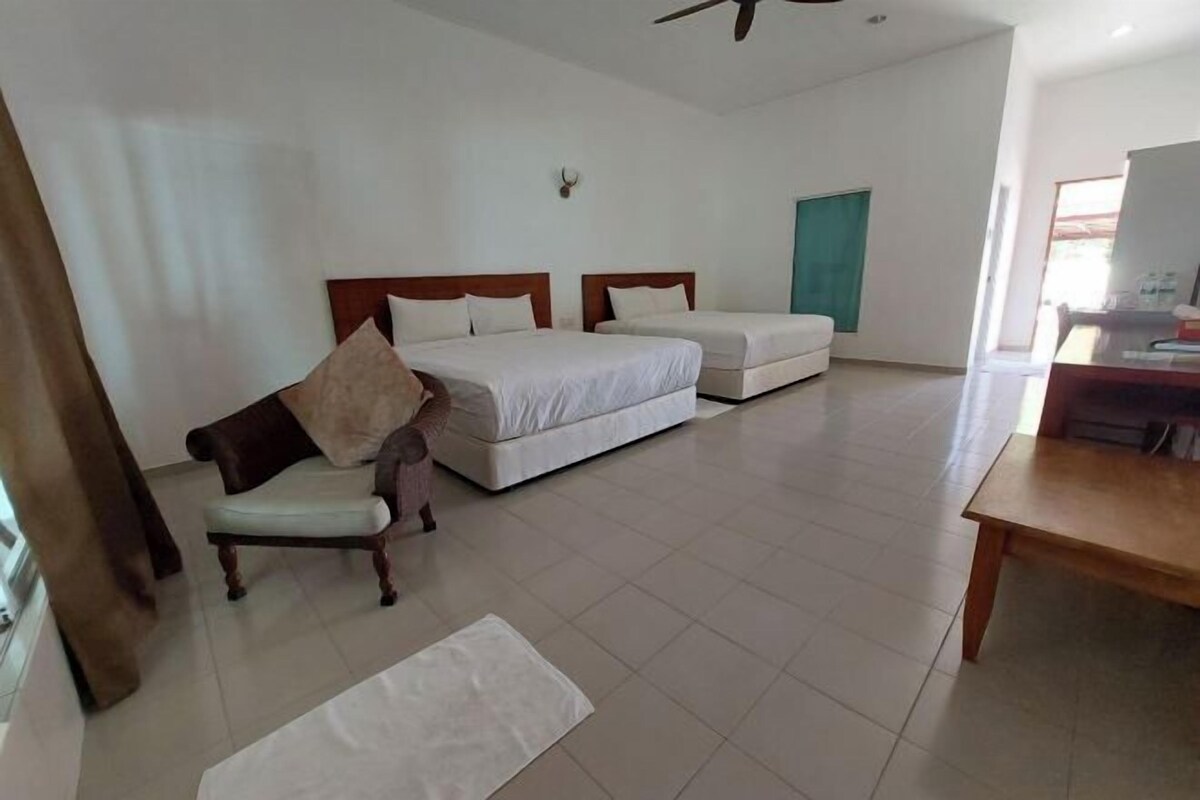 A hotel room with two single beds, a wooden chair, a small table, and a ceiling fan.