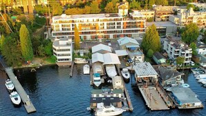 An aerial view of a marina with boats docked, a building with a sloped roof, and a dock extending into the water.
