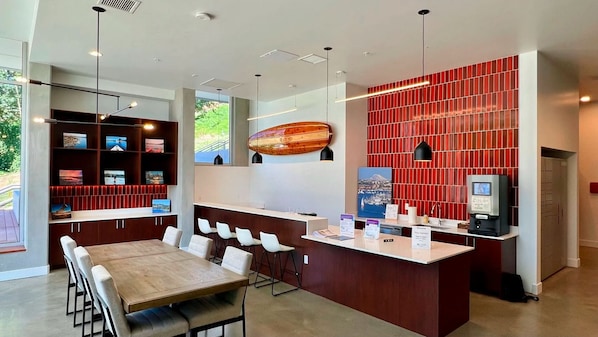 A modern hotel lobby with a wooden reception desk, a seating area with a long table and chairs, and a red-tiled wall with a surfboard decoration. - Modern 1BR Retreat – Fully Furnished, Pet-Friendly, and Minutes from Downtown (Seattle)