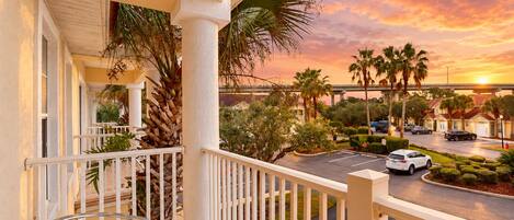 A balcony with a view of a street and palm trees during sunset.