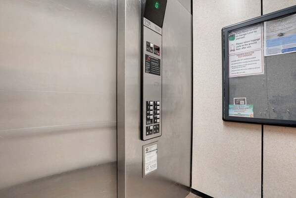 An elevator interior with a digital display, control panel, and a bulletin board with various notices. - Coastal Gem on the Golf Course w/ Shared Pool, & Beach Access - Dog-Friendly (Palm Coast)