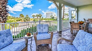A covered outdoor area with wicker furniture and a view of a beach and buildings. - Coastal Gem on the Golf Course w/ Shared Pool, & Beach Access - Dog-Friendly (Palm Coast)