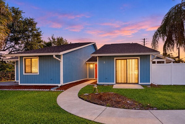 A two-story residential house with a blue exterior, a front yard with a curved pathway, and a white fence.