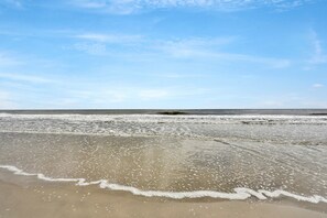 A beach with waves gently lapping onto the shore under a clear sky.