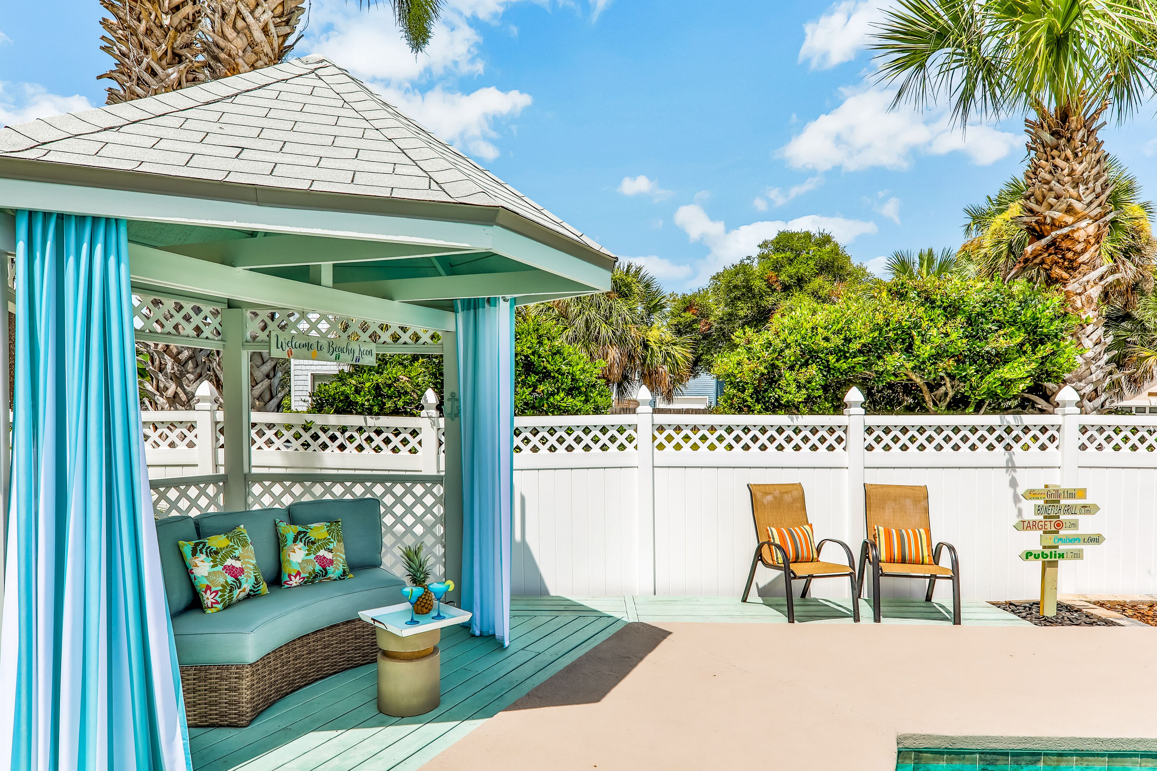 A covered outdoor seating area with a gazebo, a pool, and a white fence.