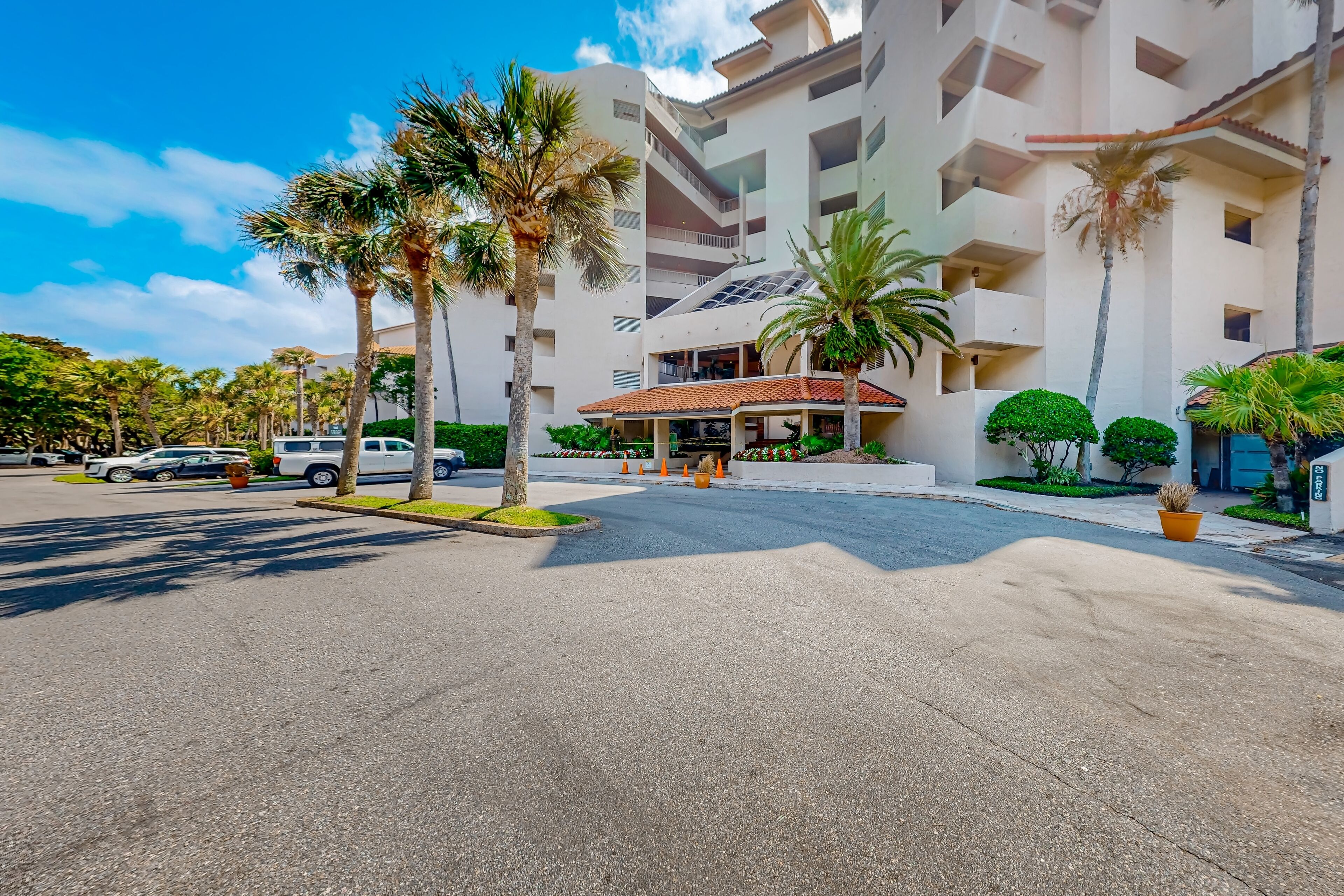Un hotel moderno con un patio central, palmeras y un acceso cubierto.