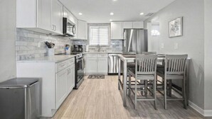 Una cocina moderna con armarios blancos, electrodomésticos de acero inoxidable y un comedor con sillas de madera.