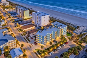 An aerial view of a coastal hotel with multiple buildings, parking areas, and a beach in the background.