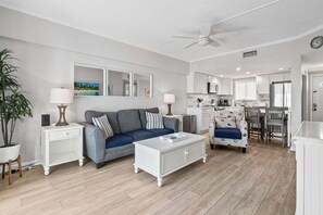 A modern living room with a sofa, coffee table, and a dining area with chairs. - Polished oceanfront condo with pool access, private balcony & washer/dryer (Jacksonville Beach)
