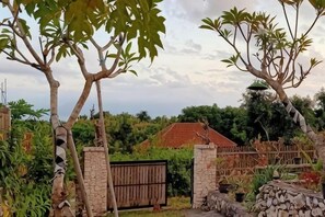 A gated property with a stone wall, a wooden gate, and a red-roofed building in the background. - Sunny Point Penida (Bali)