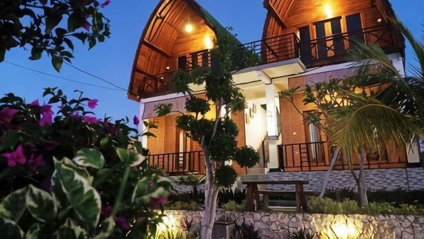 A two-story wooden house with a balcony, surrounded by greenery and flowers. - Sunny Point Penida (Bali)