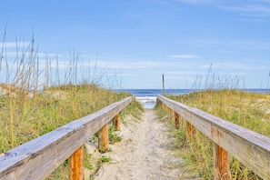 A wooden pathway leading to the beach with sand and grass on either side. - Oceanfront condo with pool, amazing view, balcony & beach access (Jacksonville Beach)