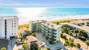 A coastal hotel with multiple floors, balconies, and a parking area. - Oceanfront condo with pool, amazing view, balcony & beach access (Jacksonville Beach)
