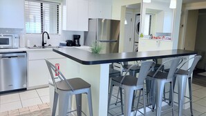 A modern kitchen with a central island, stainless steel appliances, and bar stools. - Oceanfront condo with pool, amazing view, balcony & beach access (Jacksonville Beach)