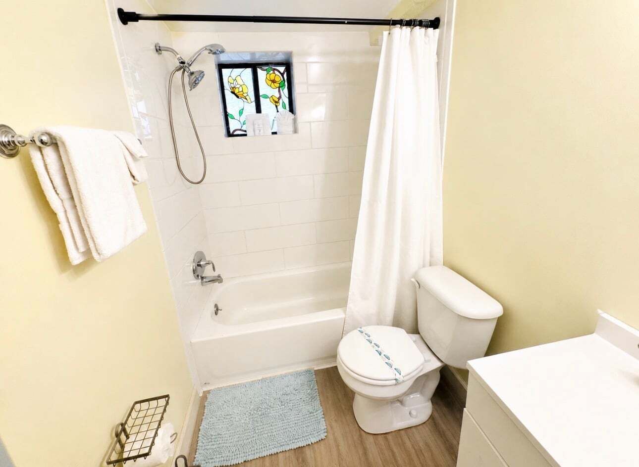 Un baño con bañera, inodoro y una pequeña ventana con diseño floral.