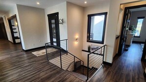 Ein geräumiger Innenraum mit Holzboden, einer Treppe mit Metallgeländer und einer Tür mit schwarzem Rahmen.