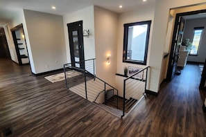 A spacious interior with a wooden floor, a staircase with a metal railing, and a door with a black frame.