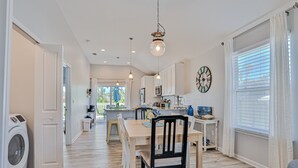 A modern kitchen with white cabinets, a dining area with a wooden table and chairs, and a laundry area with a washing machine.