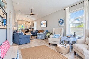 A spacious living area with a sofa set, a coffee table, and a chair. There is a dining area in the background with a table and chairs.