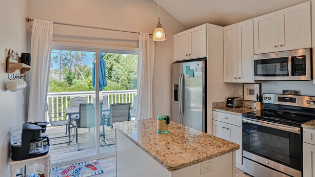 A modern kitchen with white cabinets, a stainless steel refrigerator, a microwave, and an oven. There is a small island with a glass jar on it.