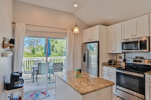 A modern kitchen with white cabinets, a stainless steel refrigerator, a microwave, and an oven. There is a small island with a glass jar on it.