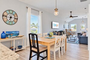A spacious living area with a dining table, chairs, a clock, and a television displaying 'CasaGo Vacation Rental'.
