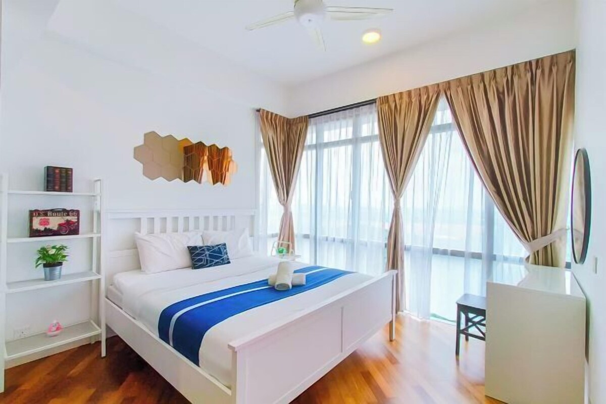A bedroom with a bed, a white wardrobe, a desk, and a large window with curtains.