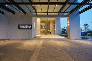 A modern hotel entrance with a sign reading 'TOWER A,' a glass facade, and a paved walkway leading to the entrance.