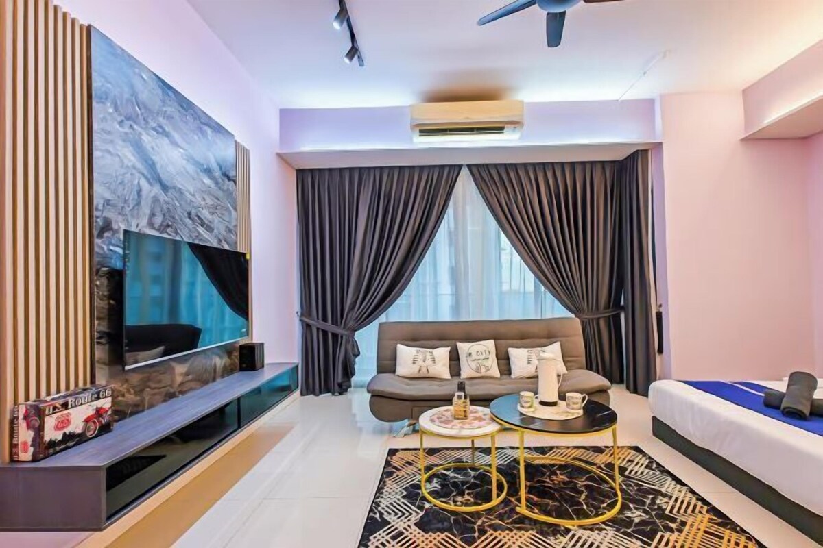 A modern hotel room with a flat-screen TV, a sofa, a coffee table, and a large window with curtains.