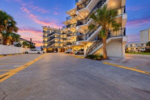 A multi-story hotel with a central courtyard, multiple balconies, and a parking area. - Oceanview condo with pool, beach access, jetted tub, W/D, & AC (Jacksonville Beach)