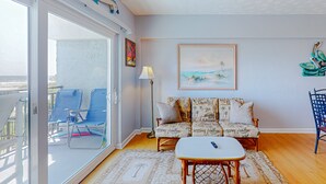 A living room with a sofa, a table, and chairs. There is a painting on the wall and a lamp.