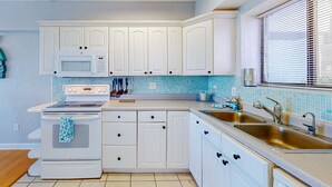 A kitchen with white cabinets, a microwave, stove, and a double sink.