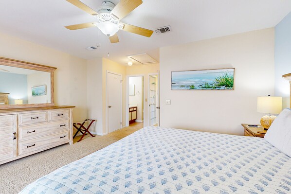 A bedroom with a bed, a ceiling fan, a dresser, a painting, and a nightstand. - Ocean-view townhome with balcony & W/D - walk to beach - dog-friendly (Jacksonville Beach)