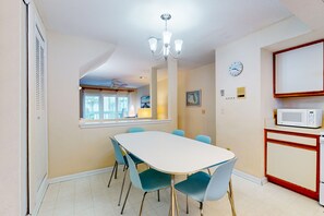 A dining area with a white table, blue chairs, a chandelier, a clock, and a microwave on a cabinet. - Ocean-view townhome with balcony & W/D - walk to beach - dog-friendly (Jacksonville Beach)
