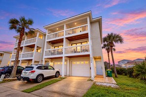 A multi-story residential building with a garage, a white car parked in front, and a well-maintained lawn. - Ocean-view townhome with balcony & W/D - walk to beach - dog-friendly (Jacksonville Beach)