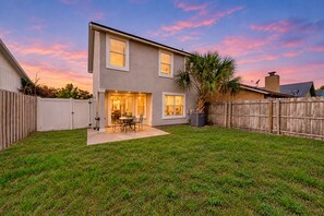 A two-story house with a patio, a wooden fence, and a palm tree.