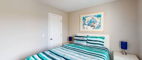 A bedroom with a bed, a nightstand, a lamp, a door, and a painting on the wall.