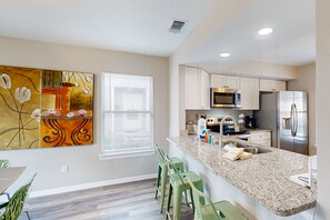 A modern kitchen with granite countertops, stainless steel appliances, and a dining area with green chairs.