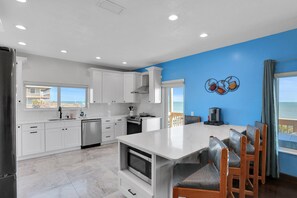 A modern kitchen with white cabinets, a central island, and a view of the ocean.