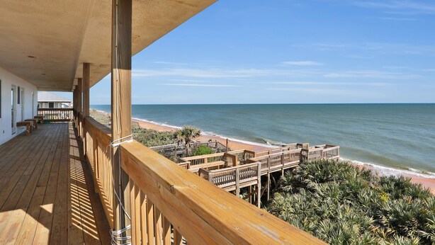 A wooden deck overlooking a beach with a wooden railing and a concrete ceiling.