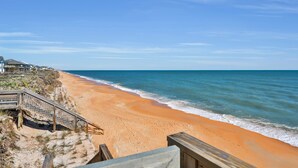 A beach with a wooden walkway leading to a building with a balcony overlooking the ocean.