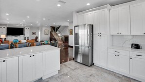 A modern kitchen with white cabinets, a stainless steel refrigerator, and a marble countertop.