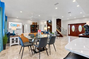 A modern living room with a glass dining table, comfortable seating, a fireplace, and a staircase leading to an upper level.