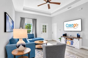 A modern living room with a sofa, armchair, and coffee table, a ceiling fan, and a TV displaying 'Casago Vacation Rentals'.