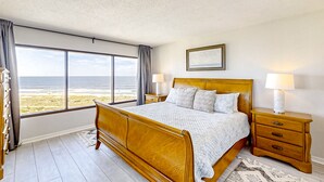 Ein Schlafzimmer mit einem Holzbett, einem Nachttisch, einer Lampe und Blick auf den Strand.