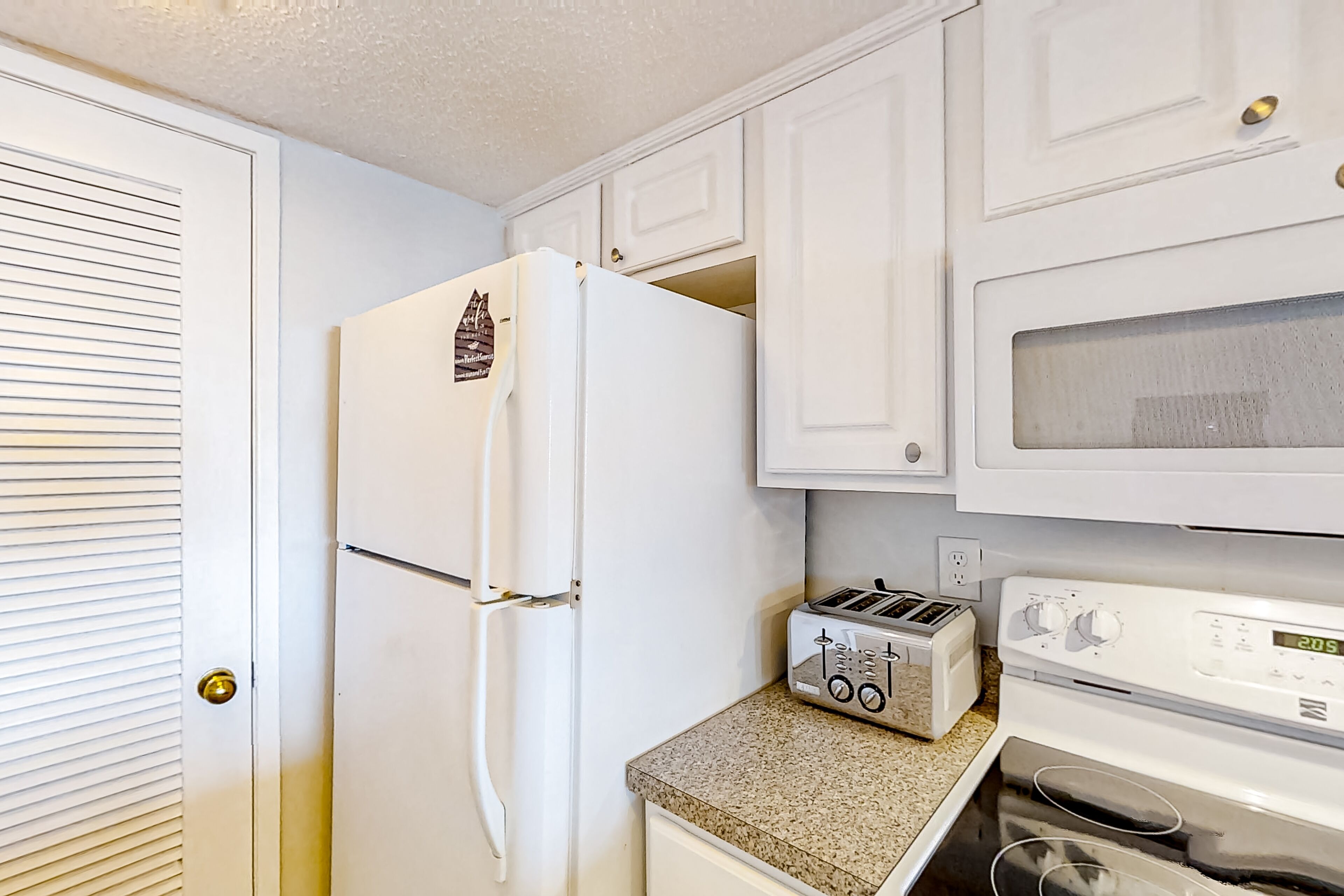 Una cocina compacta con alacenas blancas, un refrigerador, un tostador y un horno.