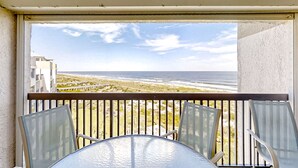 Ein Balkon mit Glastisch und Stühlen, mit Blick auf einen Strand und den Ozean.