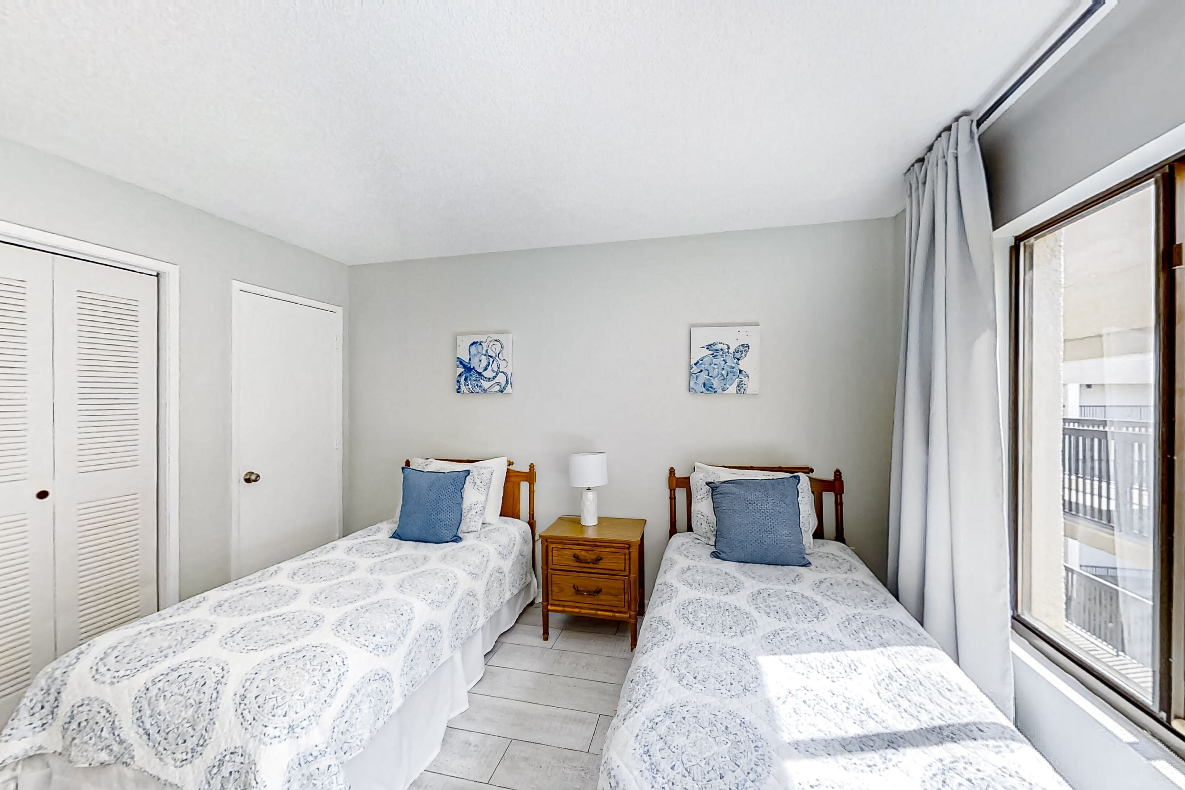A bedroom with two single beds, a nightstand with a lamp, and a window with curtains.