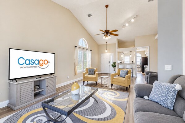 A spacious living room with a flat-screen TV, a ceiling fan, and a dining area with chairs.