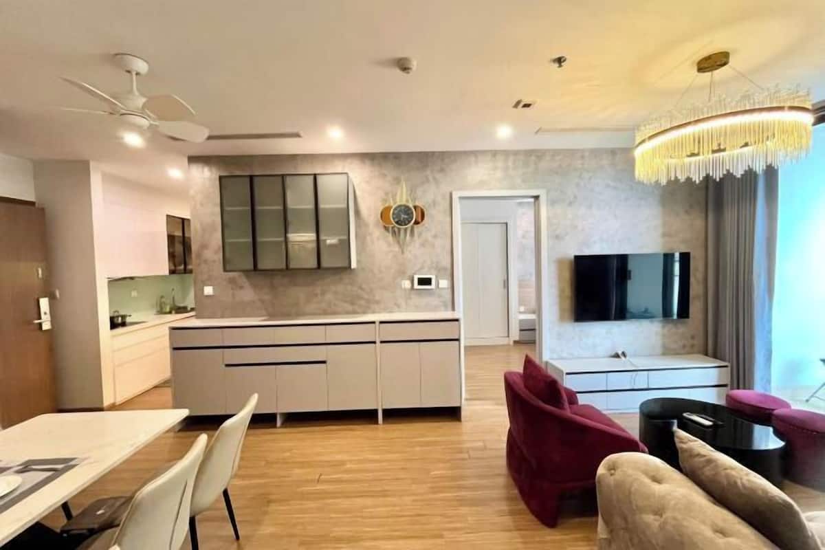 Uma sala de estar moderna com área de jantar, cozinha e televisão fixada na parede.